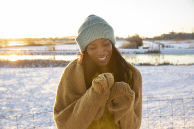 Cheerful mature woman wearing blue knit hat standing on snow during winter