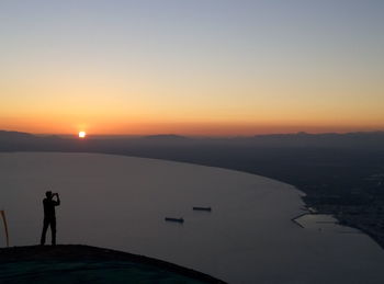 Silhouette of man standing on lake during sunset