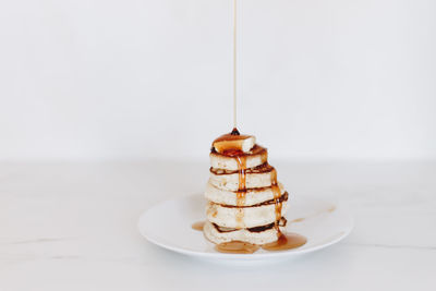 Syrup being poured on a stack of pancakes in a white kitchen scene.