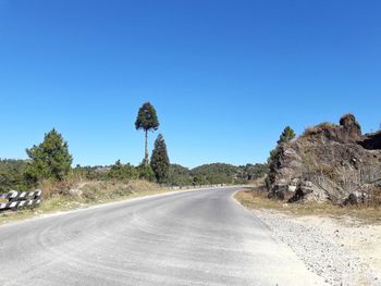 Road amidst trees against clear blue sky