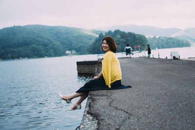 Woman sitting on riverbank against mountains