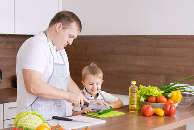 Happy family father with son preparing vegetable salad at home, vegetables