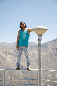 Full length of man standing on railing against mountains and clear sky