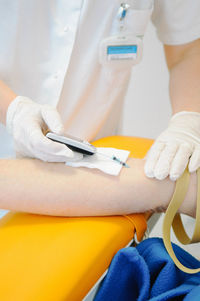 Midsection of doctor drawing blood sample from arm for test at hospital