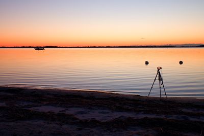 Silhouette of tall nature photographer at tripod taking picture on the beach at sunset time