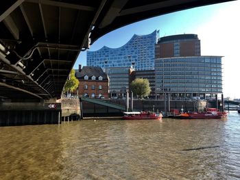 Bridge over river by buildings in city against sky