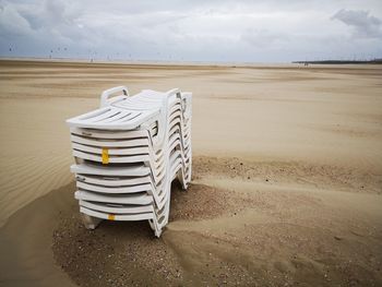 Empty deck chairs on sand at beach against sky