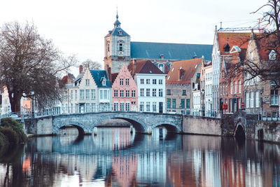 Arch bridge over river by buildings in city against sky