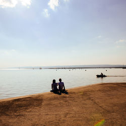 Rear view of couple sitting on calm sea