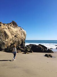 Rear view of woman walking at beach on sunny day
