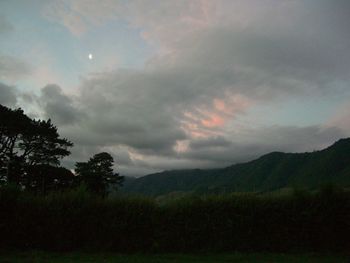 Silhouette of trees on field against cloudy sky