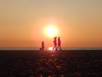Silhouette people walking at beach against orange sky