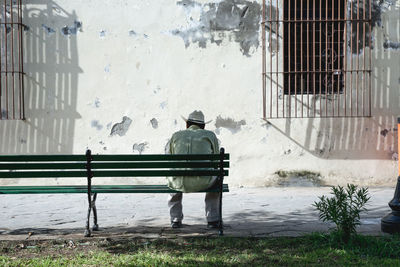 Rear view of man sitting on bench against building