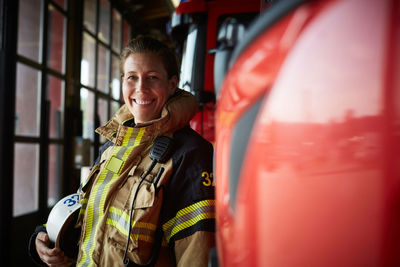Portrait of smiling female firefighter standing by fire engine at fire station