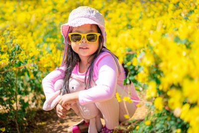 Portrait of cute girl wearing sunglasses crouching in flowering plants