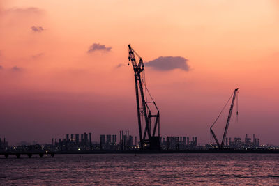 Silhouette cranes against sky during sunset