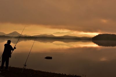 Silhouette man fishing in lake against sky during sunset