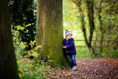 Boy standing by moss covered tree in forest