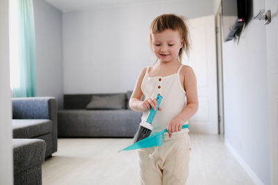 Cute european child with blue scoop for garbage and brush for sweeping floor helps to clean