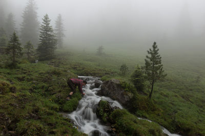 Side view of man bending by stream during foggy weather