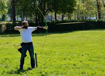 Full length of man shooting arrow on grassy field during sunny day