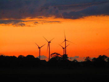 Silhouette windmills on landscape against romantic sky at sunset