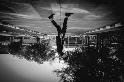 Upside down image of man hanging by tree against sky