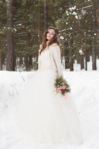 Beautiful bride in a white dress with a bouquet in a snow-covered winter forest. 