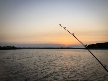 Silhouette fishing rod on sea against sky during sunset