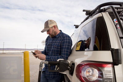 Mid adult man using smart phone while standing by car at gas station