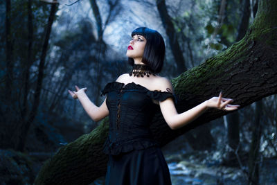 Woman standing by tree trunk in forest