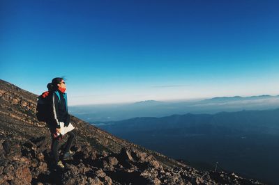 Woman standing on mountain against clear blue sky