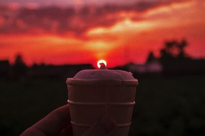 Close-up of hand holding ice cream cone against sky during sunset
