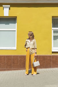 Full length of woman standing against yellow wall