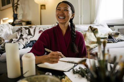 Happy young woman with book herbs at table