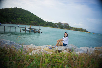 Young woman sitting on shore against sky