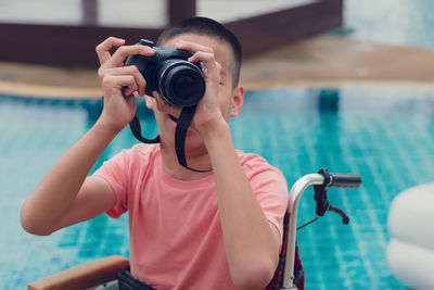 Cheerful boy photographing through camera by swimming pool