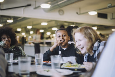 Friends laughing while having food at table during lunch break in cafeteria