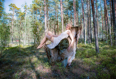 A woman in a white dress lies on a tree in the middle of the forest and merges with nature