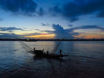 Silhouette people in river against sky during sunset