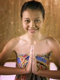 Portrait of smiling young woman with hands clasped sitting at spa