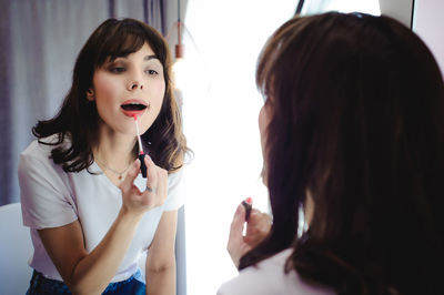 Close-up of young woman applying red lipstick in front of mirror at home