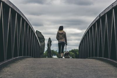 Rear view of woman walking on bridge against sky