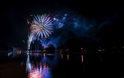 Low angle view of firework display by river at night