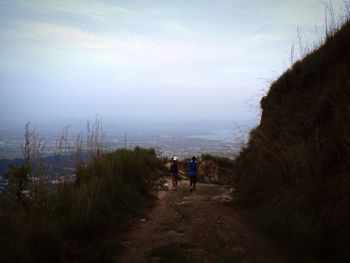 People walking on road amidst trees against sky