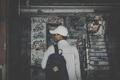 Rear view of man standing by graffiti on wall