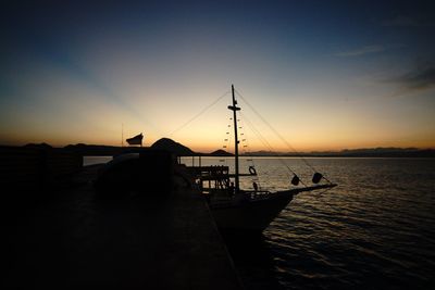 Silhouette sailboats moored on sea against sky during sunset