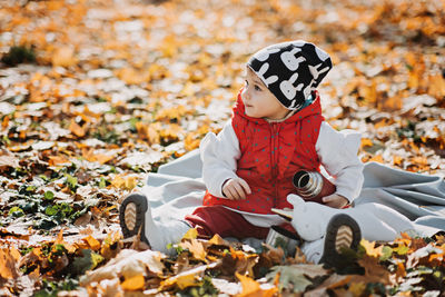 Little cute girl drinks tea from a thermos in the autumn park. cute little toddler baby with