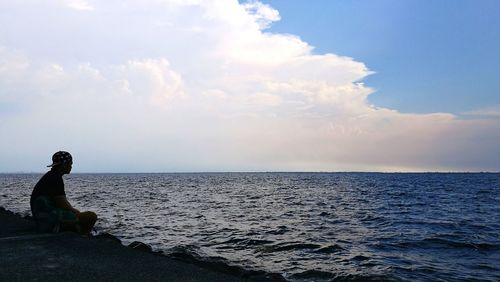 Side view of man sitting on sea against sky