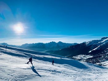 People skiing on snowcapped mountain against sky during winter